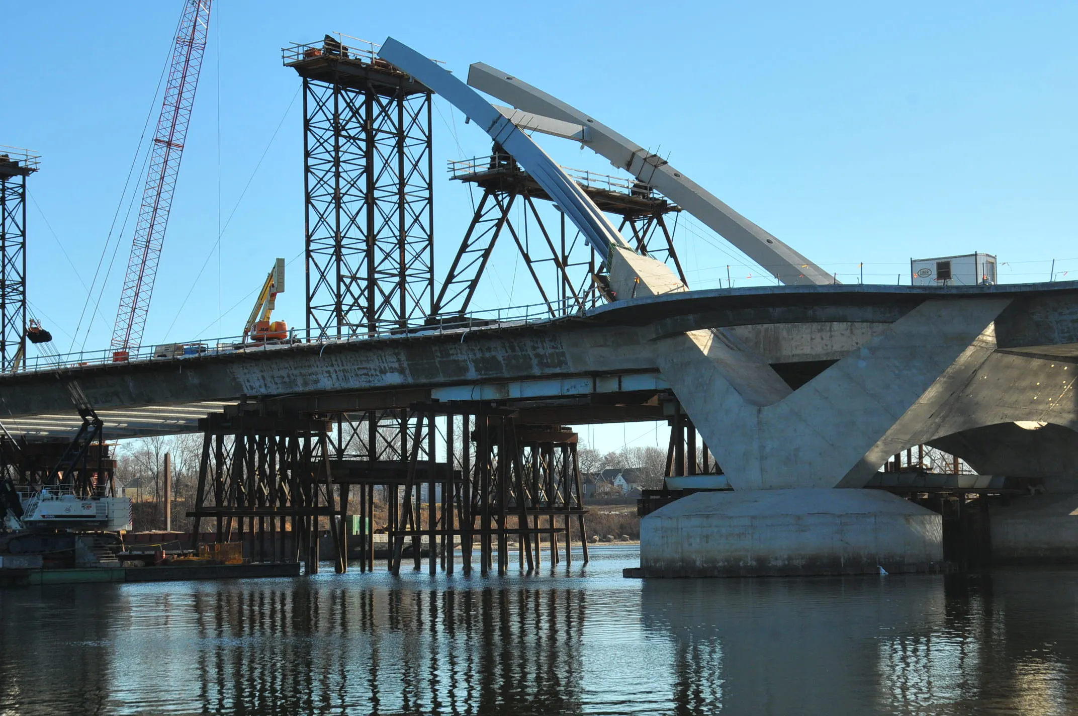 Large concrete and steel bridge under construction over a river, with visible cranes and temporary support structures.