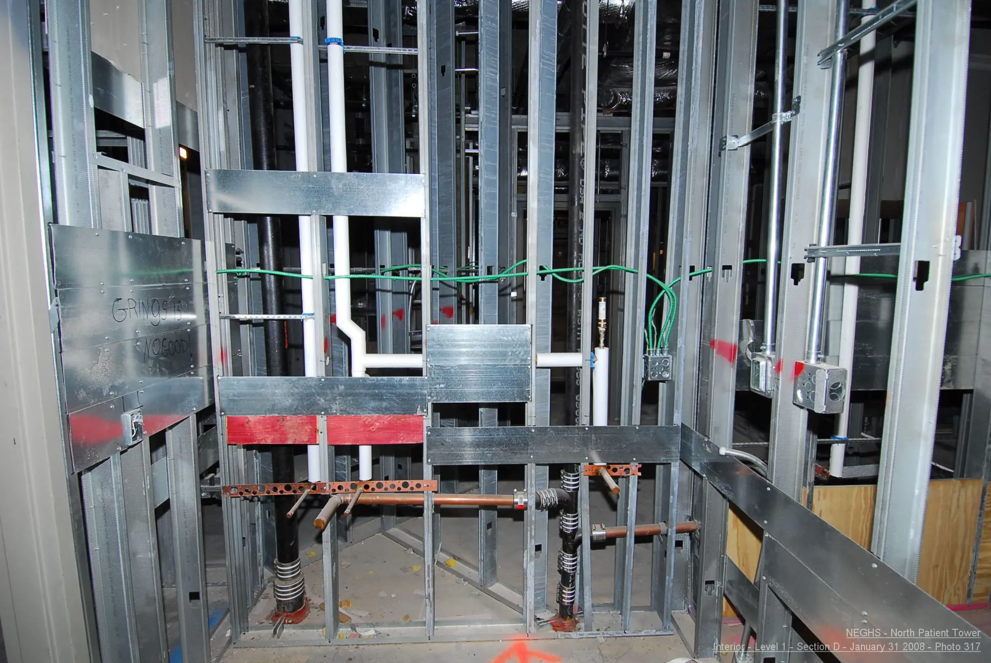 Construction site with exposed metal studs, pipes, and electrical conduit during rough-in.