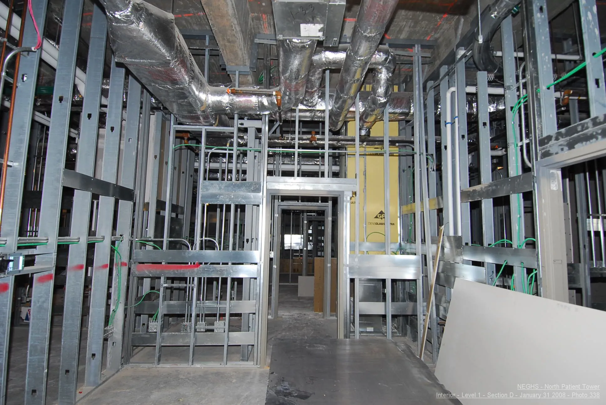New hospital patient tower construction showing bare metal stud walls, HVAC, plumbing, and electrical lines.