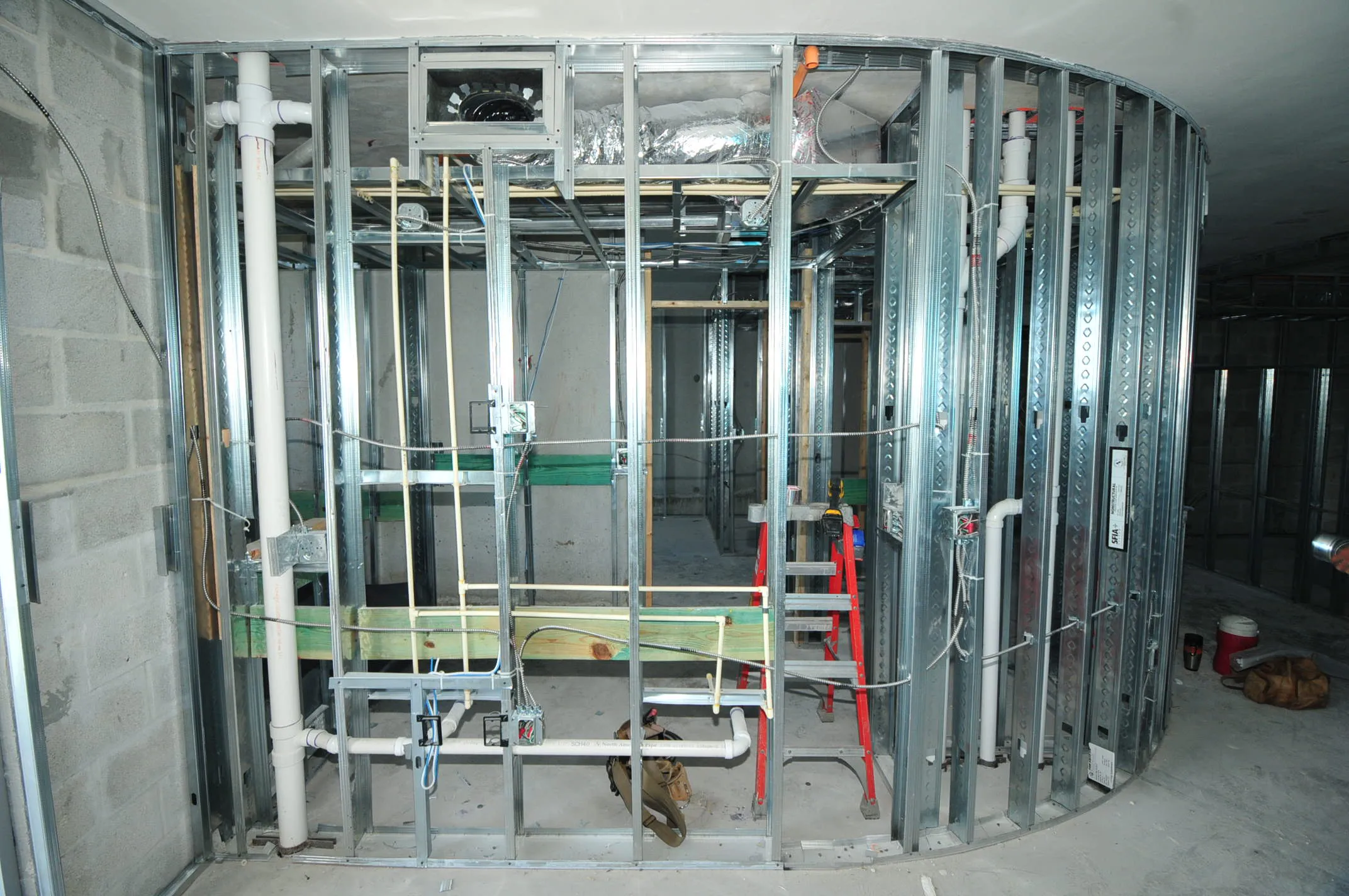 Building interior during rough-in construction, featuring metal stud framing, plumbing, HVAC, and electrical.