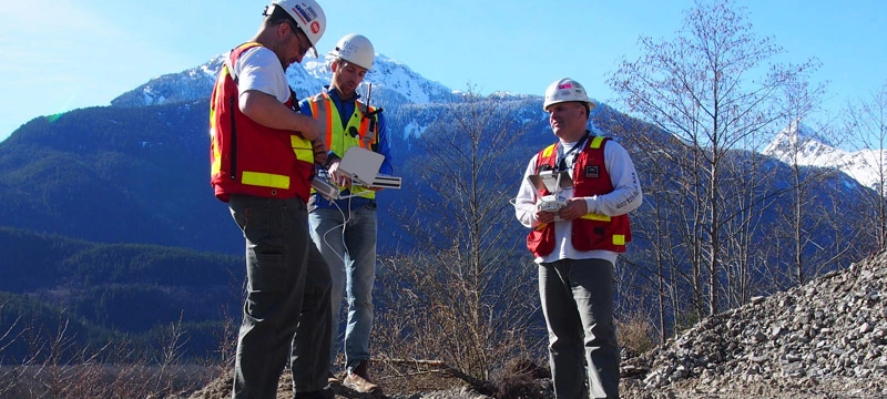 Construction team surveying mountain site with drones for risk management.