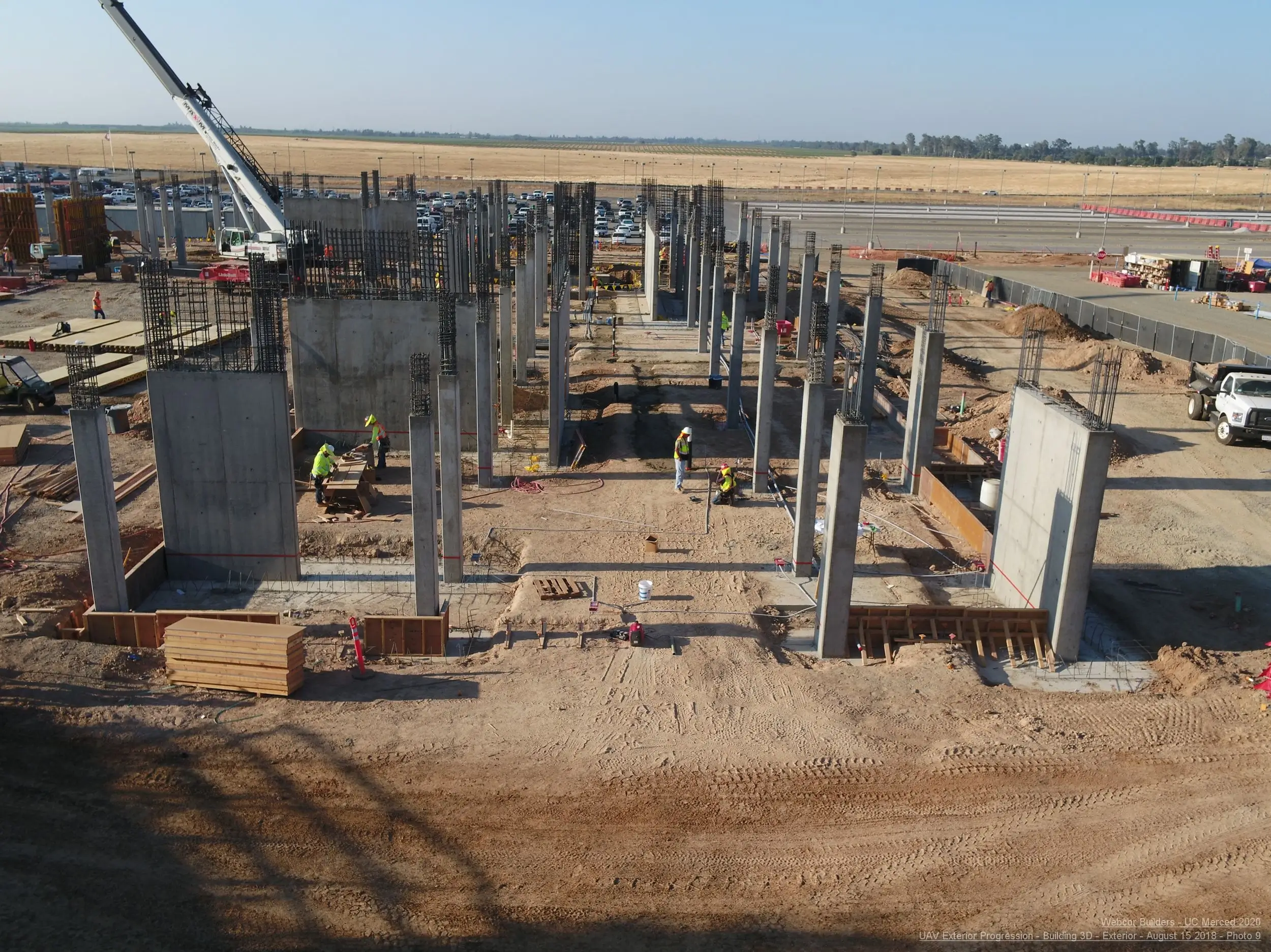UAV mapping perspective of a large construction site with concrete structures, workers, and a crane.