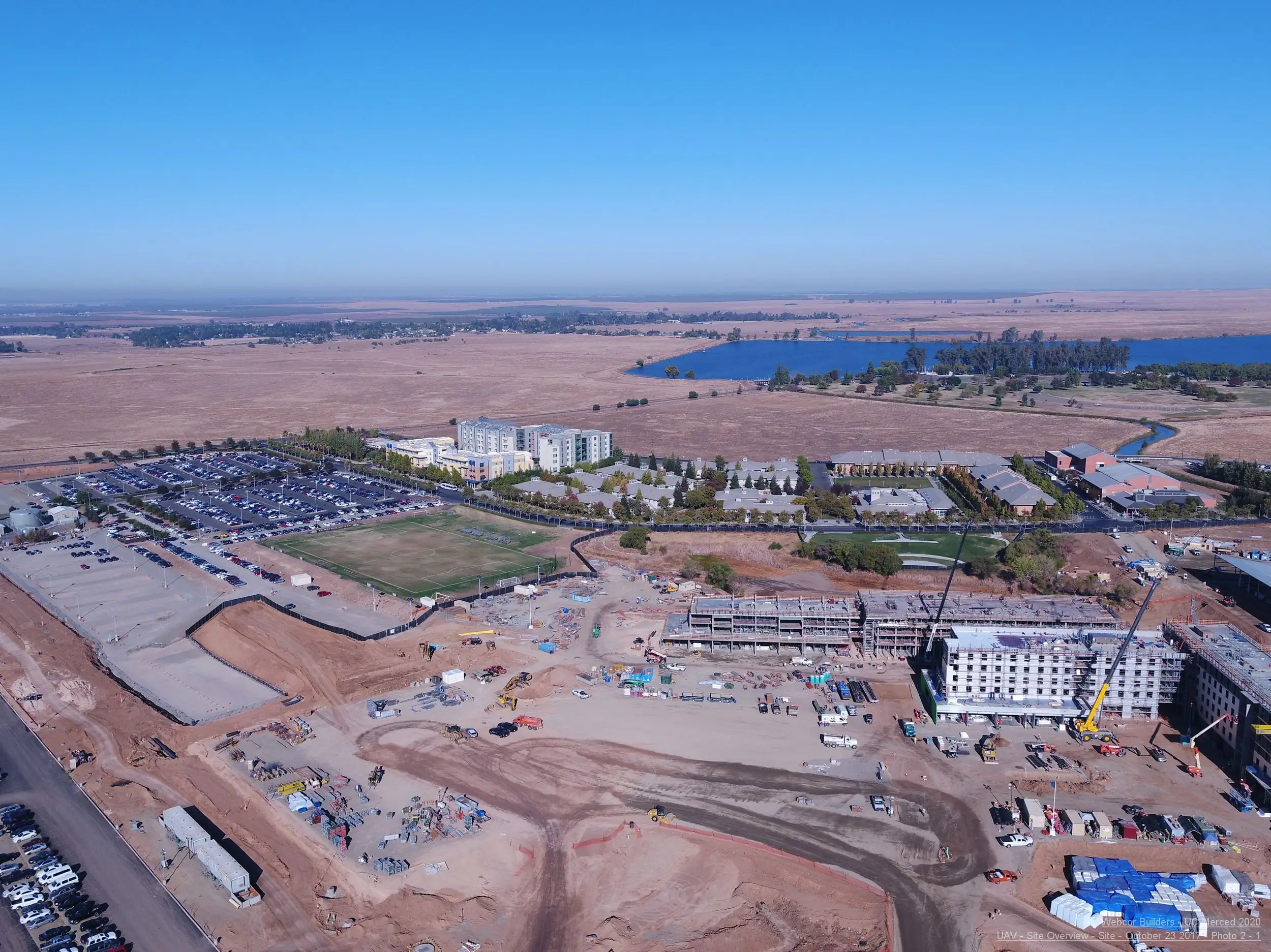 UAV mapping shows an extensive construction site, campus buildings, and a lake under a clear sky.