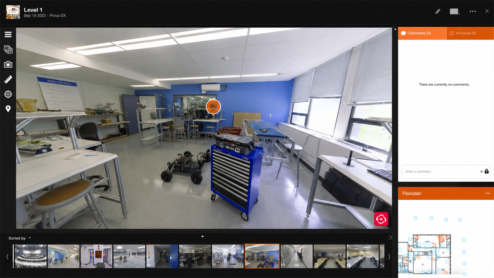 Panoramic view of a bright engineering lab with workbenches, a blue tool cabinet, and a robotic car chassis.