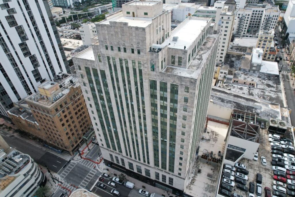 High angle view of a tall, light-colored skyscraper with numerous vertical window panes amidst a bustling city.