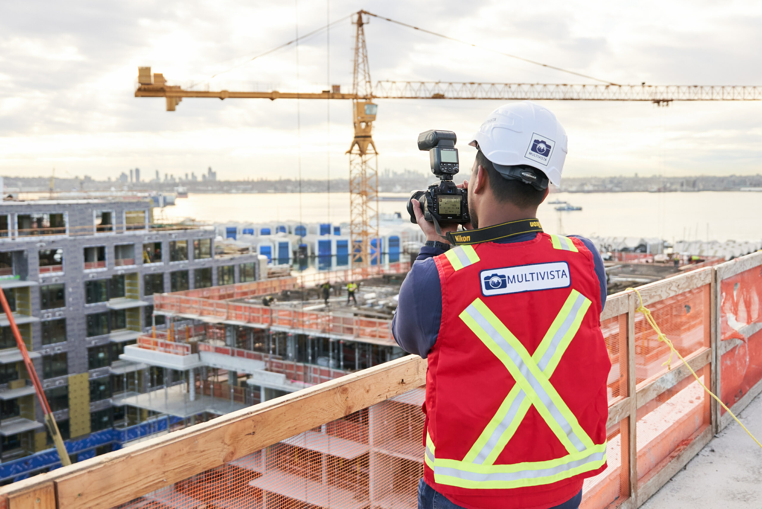 Multivista photographer in hard hat & safety vest captures construction site, buildings, crane, and city skyline.