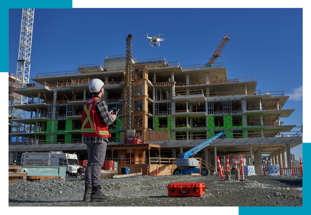 Construction worker flying drone over a building site with cranes.