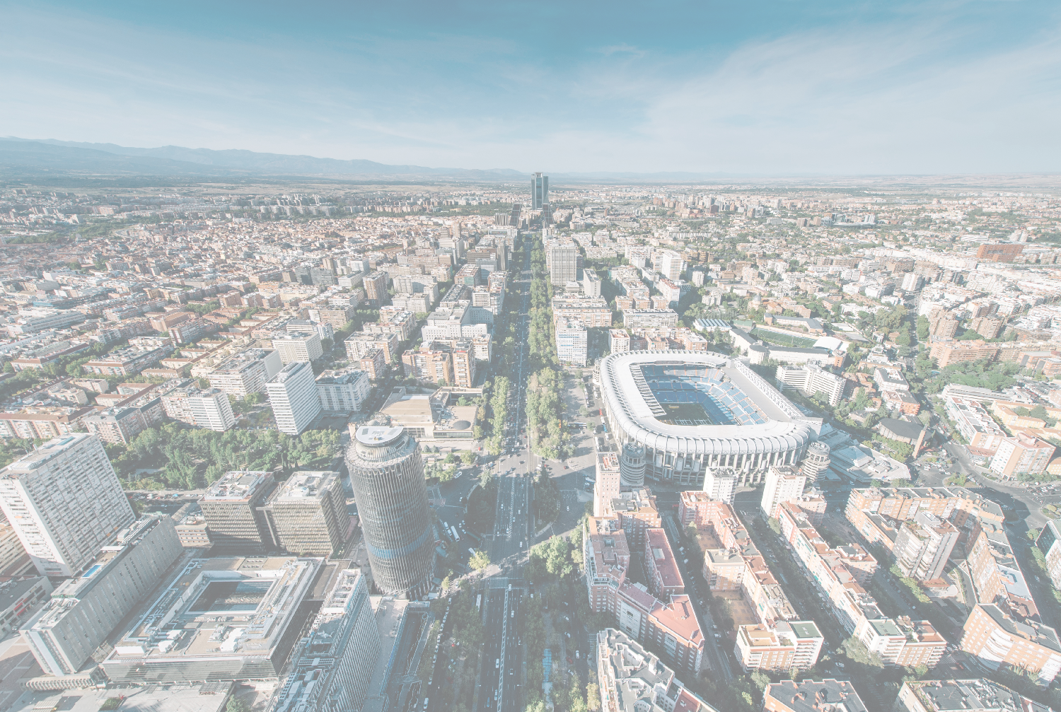 Aerial view of Madrid with Santiago Bernabéu stadium, a tree-lined boulevard, and skyscrapers.