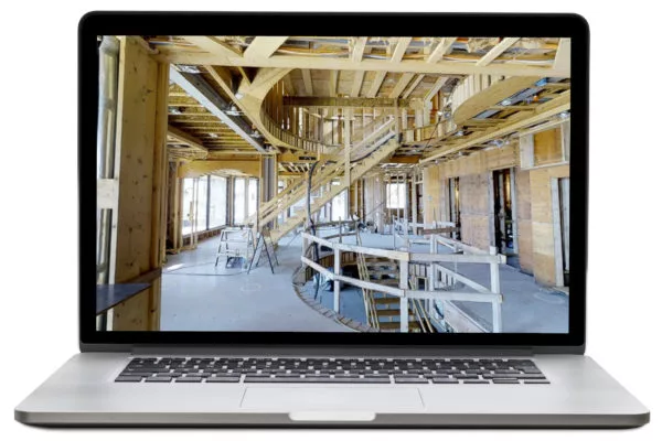 Laptop displaying a 3D model of a house interior under construction with exposed wood framing and a curved staircase.
