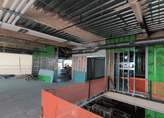 Multilevel construction interior with exposed metal studs, green sheathing, and safety netting.