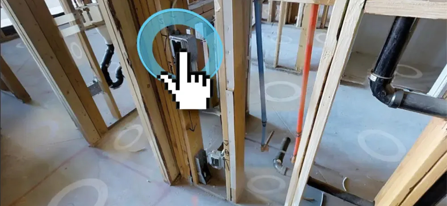 Virtual inspection of a building rough-in, with a hand cursor highlighting an electrical box among wooden studs and pipes.
