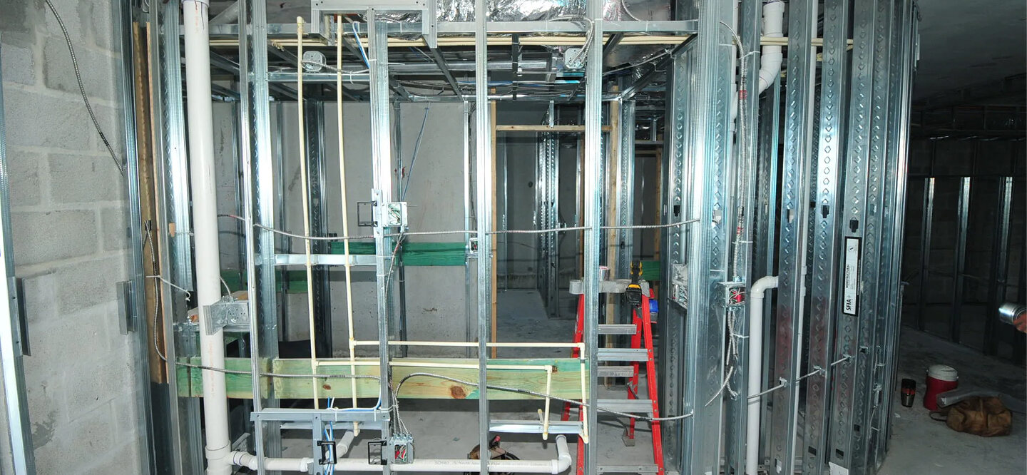 Interior view of new building construction with metal stud walls, exposed plumbing, and electrical rough-in.