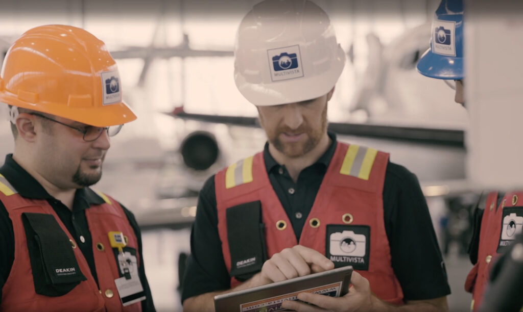 Multivista team members in hard hats and safety vests review data on a tablet at a job site.