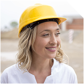 Smiling woman in a yellow hard hat looking right at a construction site.