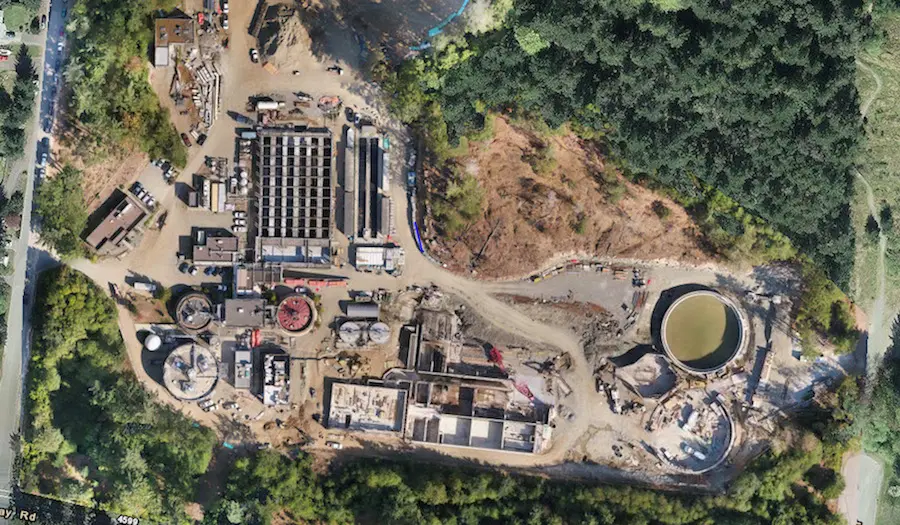 Aerial view of a wastewater treatment plant construction site with circular tanks and various buildings.