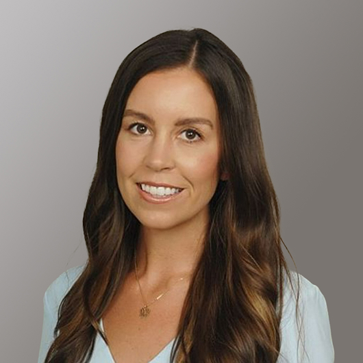 Smiling woman with long brown hair wearing a light blue top and a necklace.