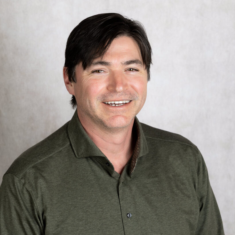 Smiling man with dark hair wearing a dark green collared shirt.
