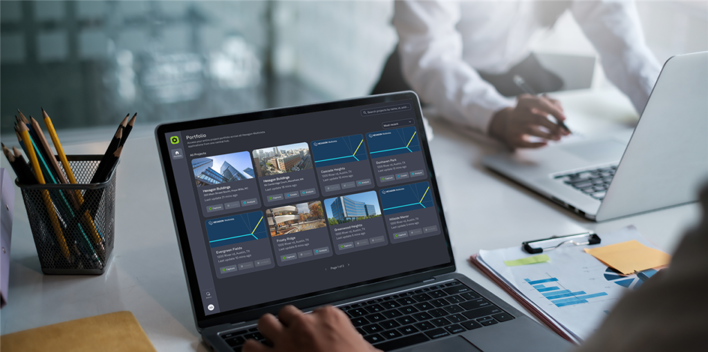 Person typing on a laptop displaying a project portfolio application with building designs. Another person works nearby.