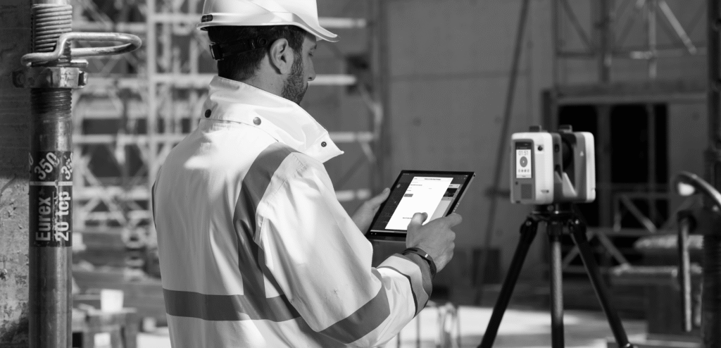 Engineer uses tablet with 3D laser scanner on tripod for construction site survey.