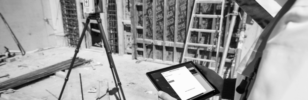 Construction worker uses a tablet on site with a laser scanner, rebar, and concrete formwork.