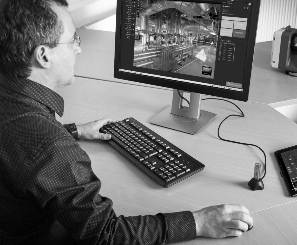 Man in glasses viewing a complex 3D industrial facility model on a computer, using a keyboard and mouse.