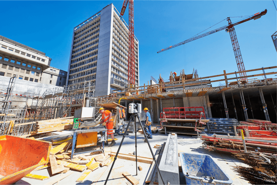 Workers on a large construction site with a high-rise building, cranes, and a laser scanner under clear skies.