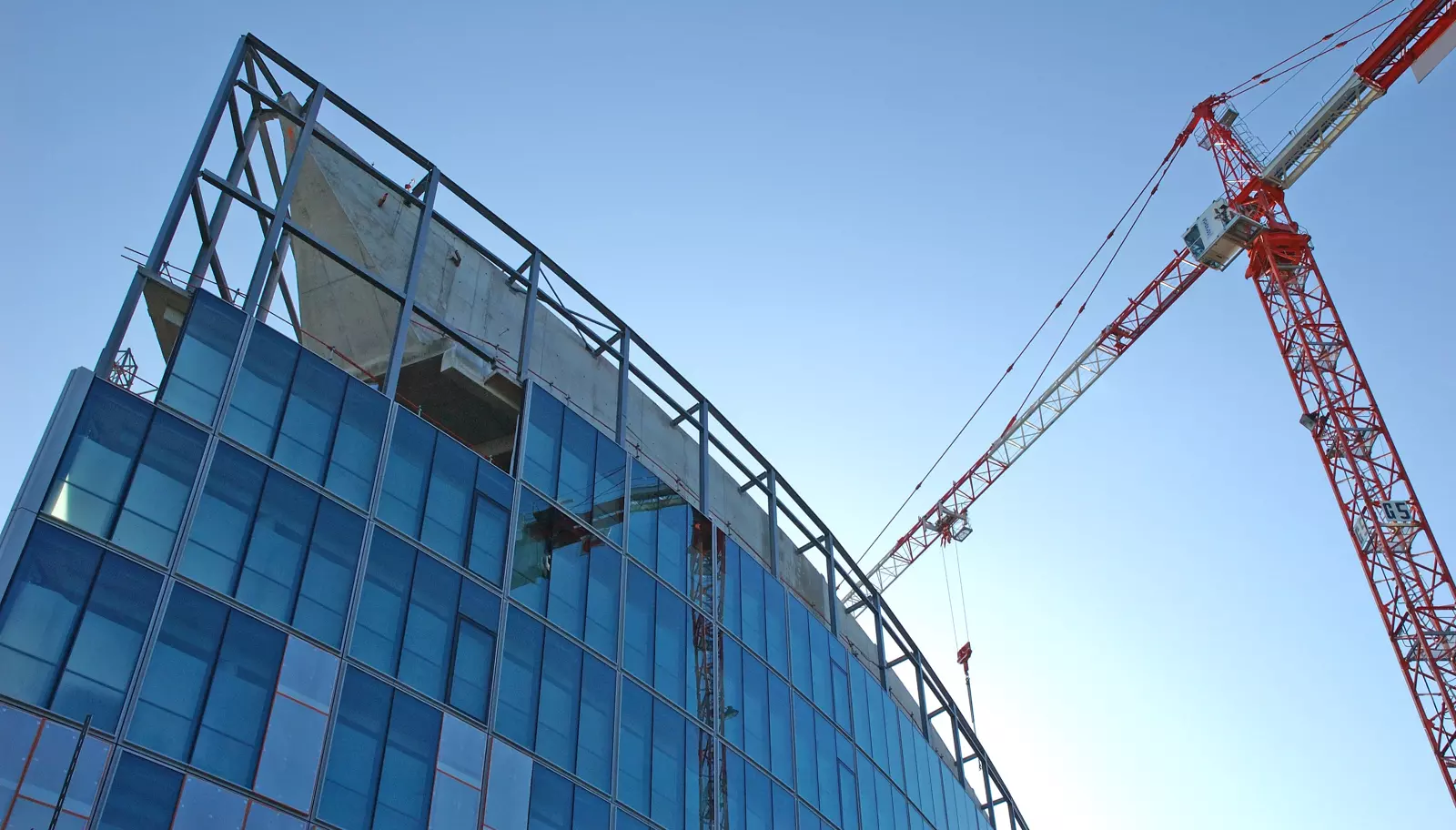 Modern building construction with blue glass facade and a large tower crane against a clear blue sky.