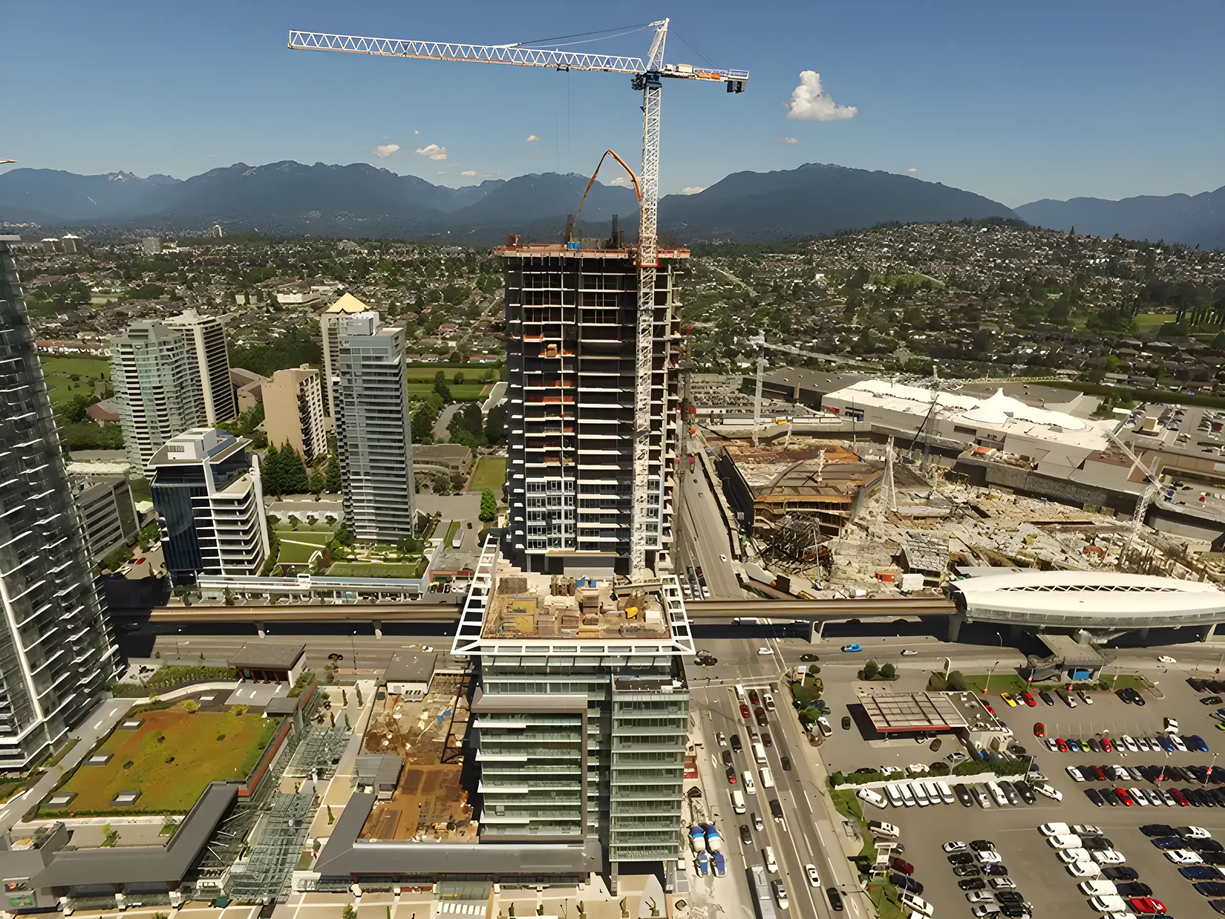 Aerial view of a city with a tall skyscraper under construction, a crane, and mountains in the background.