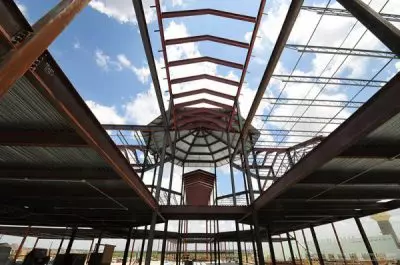 Steel framework of a large building under construction with an octagonal center against a blue sky.