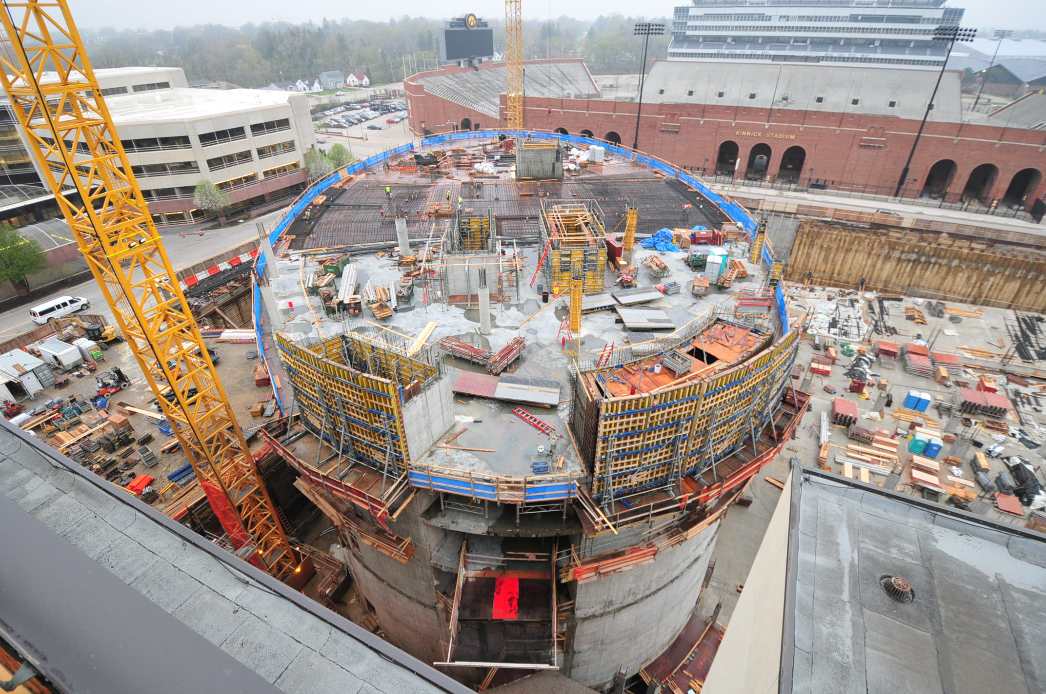 Overhead view of a circular building construction site with a yellow crane, scaffolding, and Kinnick Stadium in the distance.