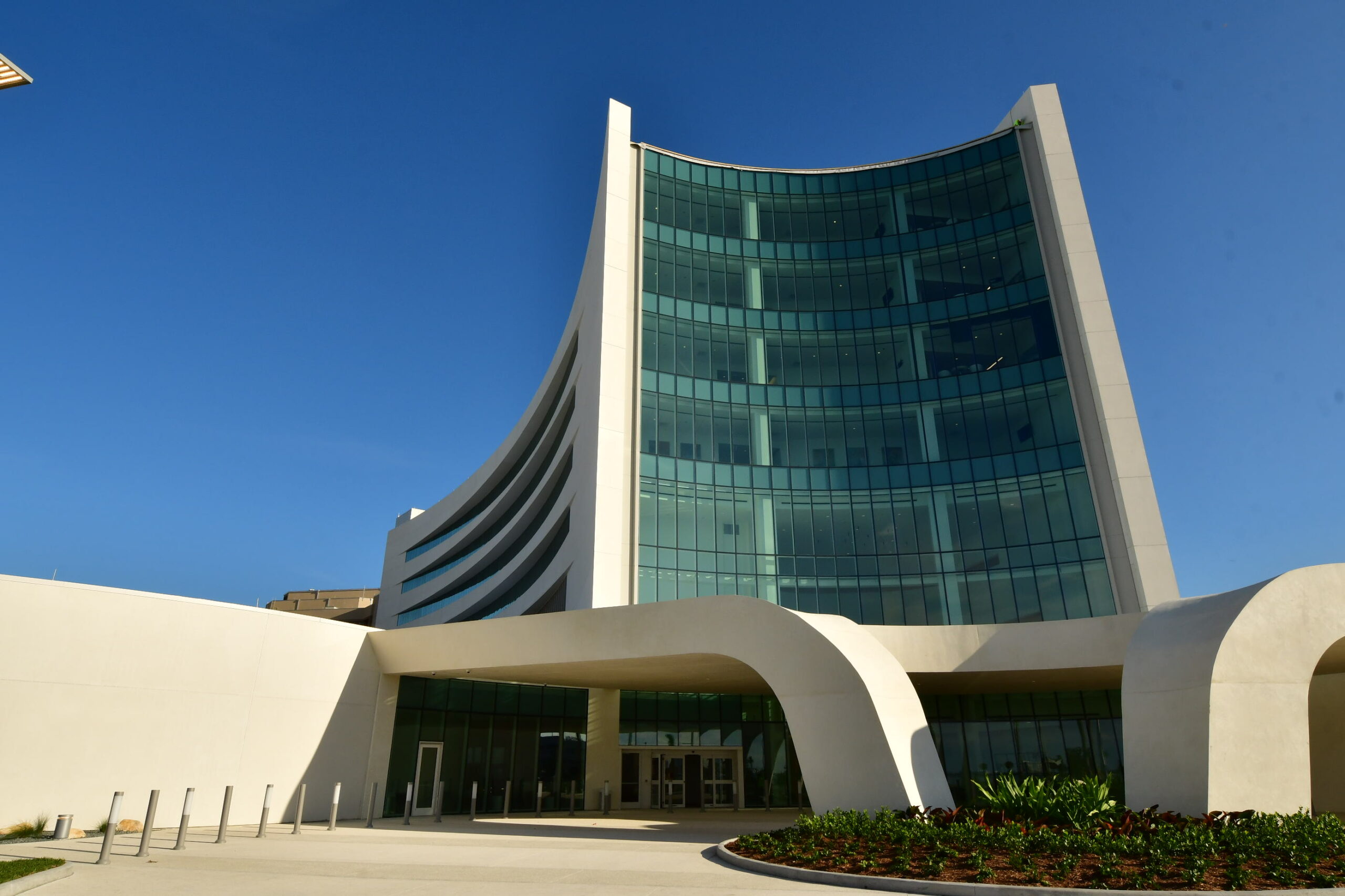 Modern, curved building with glass facade and arched entrance under a clear blue sky.