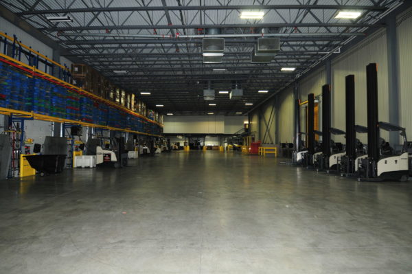 Large, clean warehouse with stacked products on high shelves and multiple forklifts ready for work.