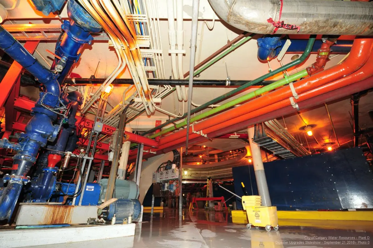 Industrial water treatment facility interior with colorful pipes, large pumps, and a reflective wet floor.