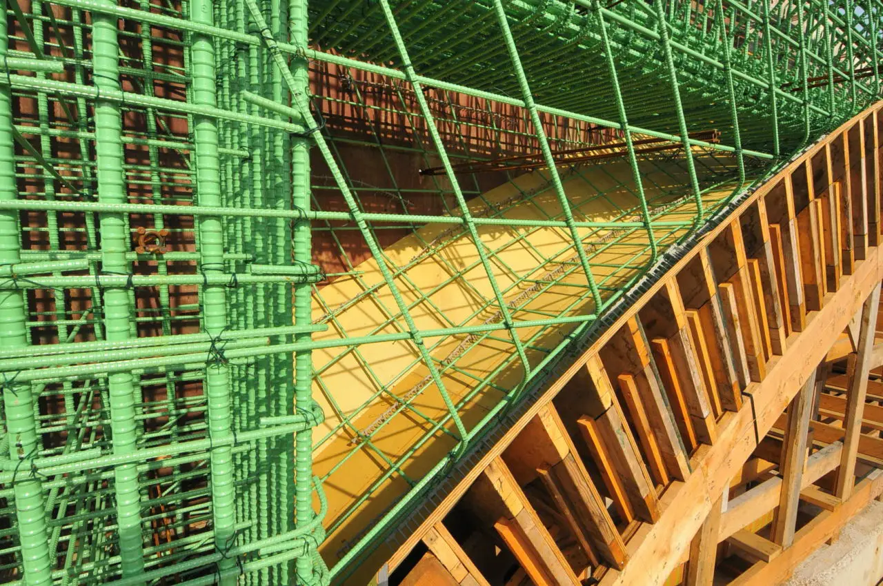 Green rebar grid and wooden formwork for a concrete structure under construction.