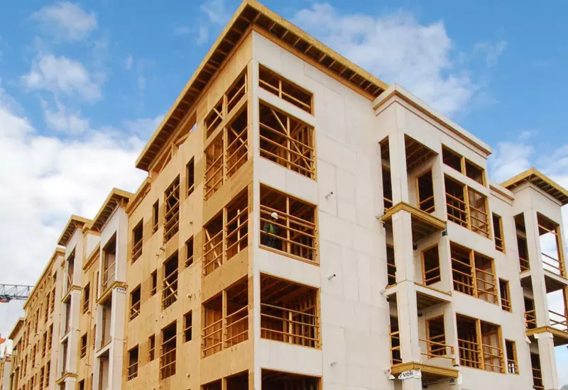 Multi-story building under construction with wood framing and partial exterior sheathing under a blue sky.