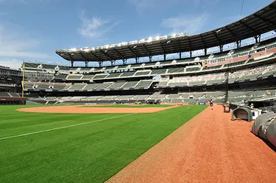 Baseball stadium with green grass field, dirt path, and empty tiered seating.