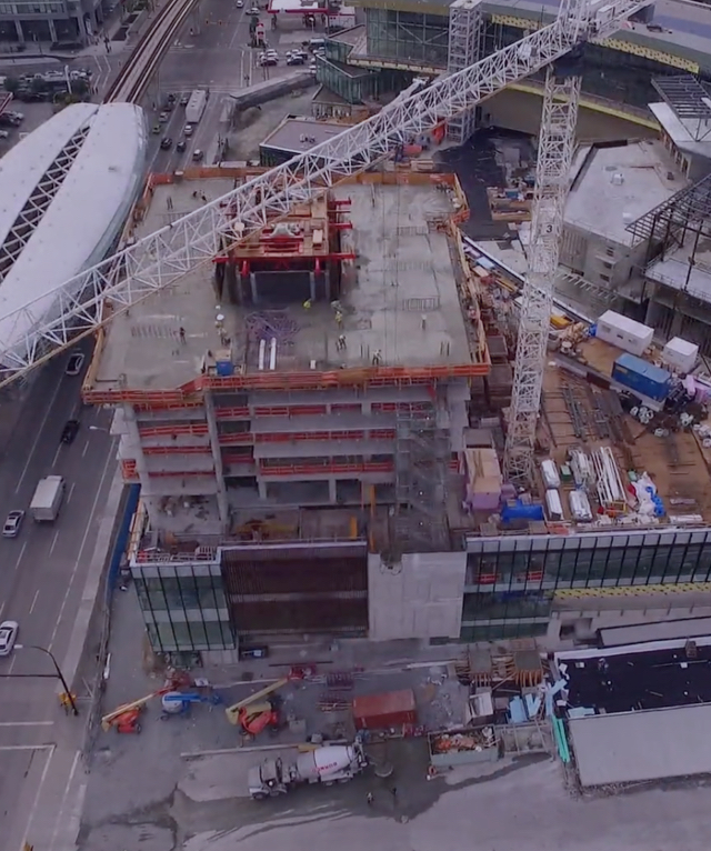 Aerial view of a multi-story building under construction with a large tower crane, active work site, and urban street.