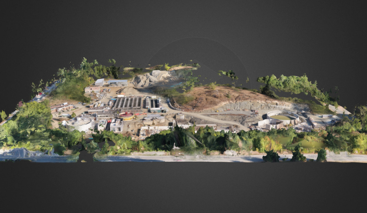 Aerial 3D scan of a large construction site with multiple buildings and tanks amidst green hills.