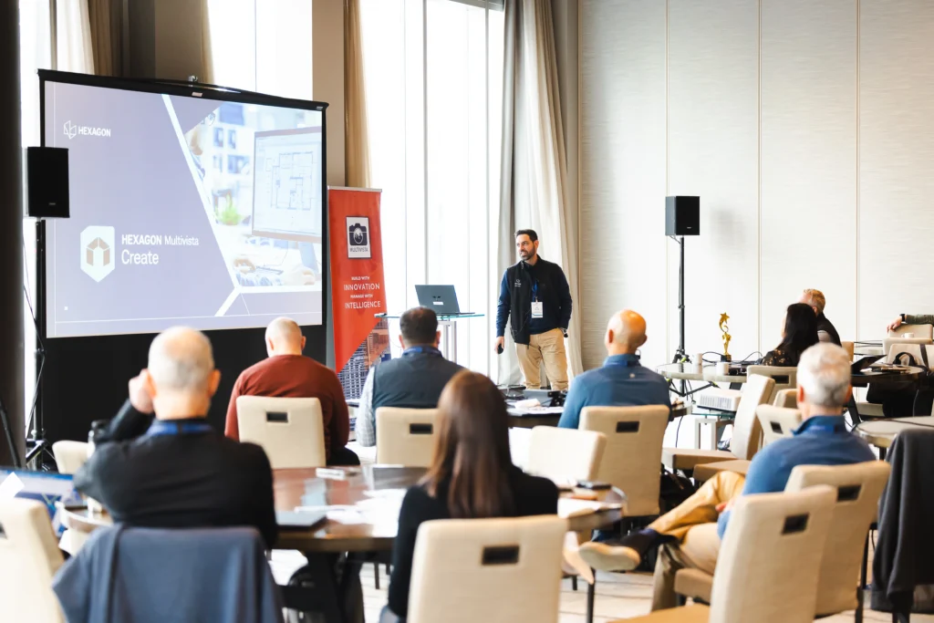 Speaker presents Hexagon Multivista Create software on a large screen to an attentive audience at a conference.