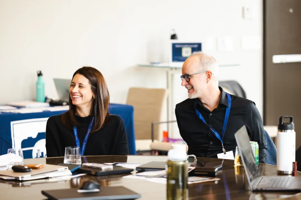 Two smiling professionals with lanyards engaged in a lively discussion at a conference or meeting.
