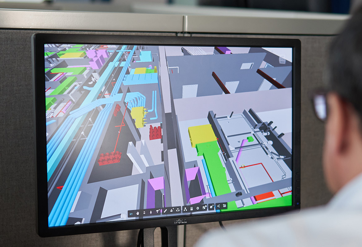 Engineer reviews a complex 3D BIM model on a computer screen, showing detailed building systems and design.