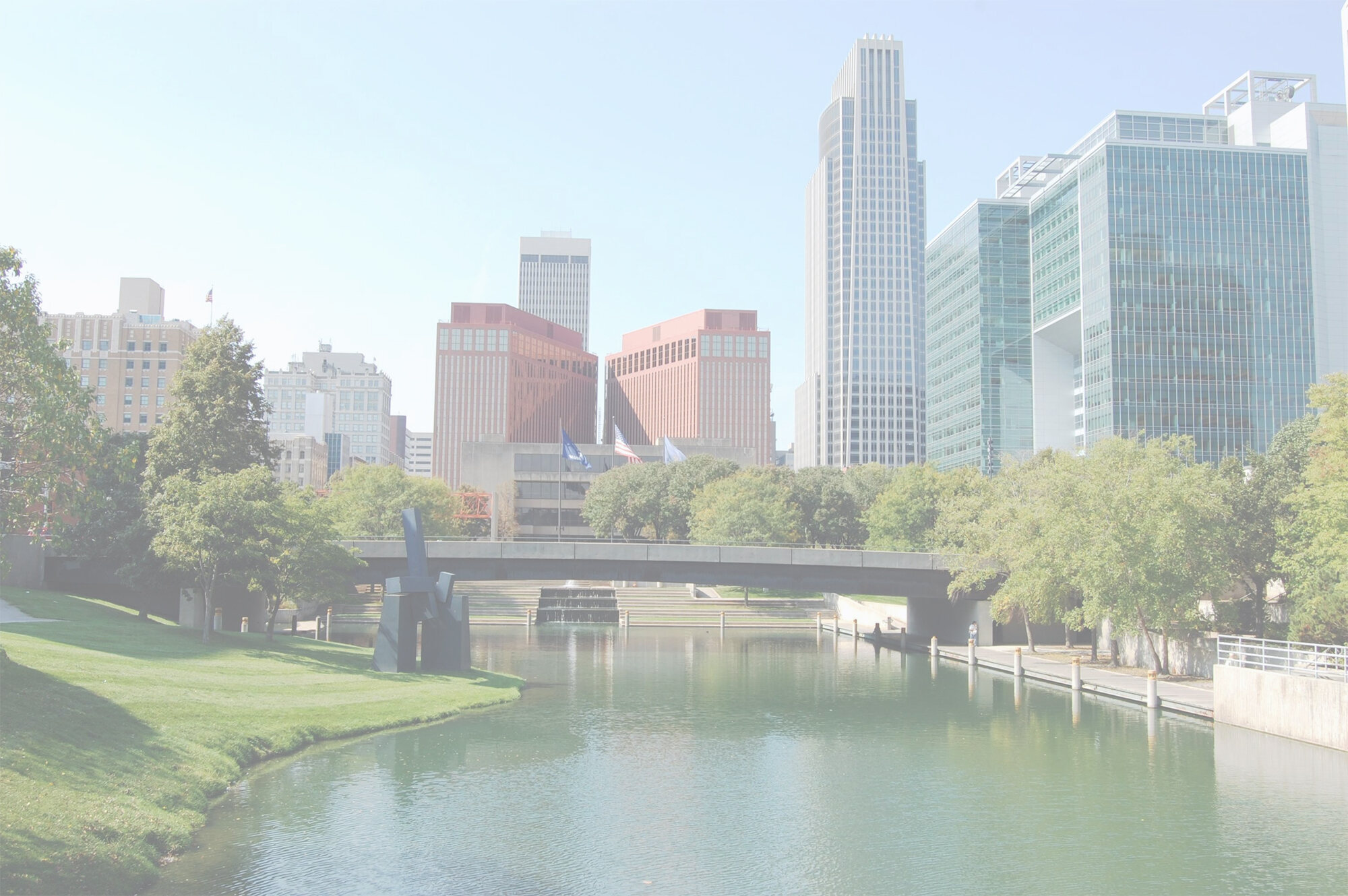 Omaha skyline with a tranquil canal, lush green park, a bridge, and diverse architectural buildings.
