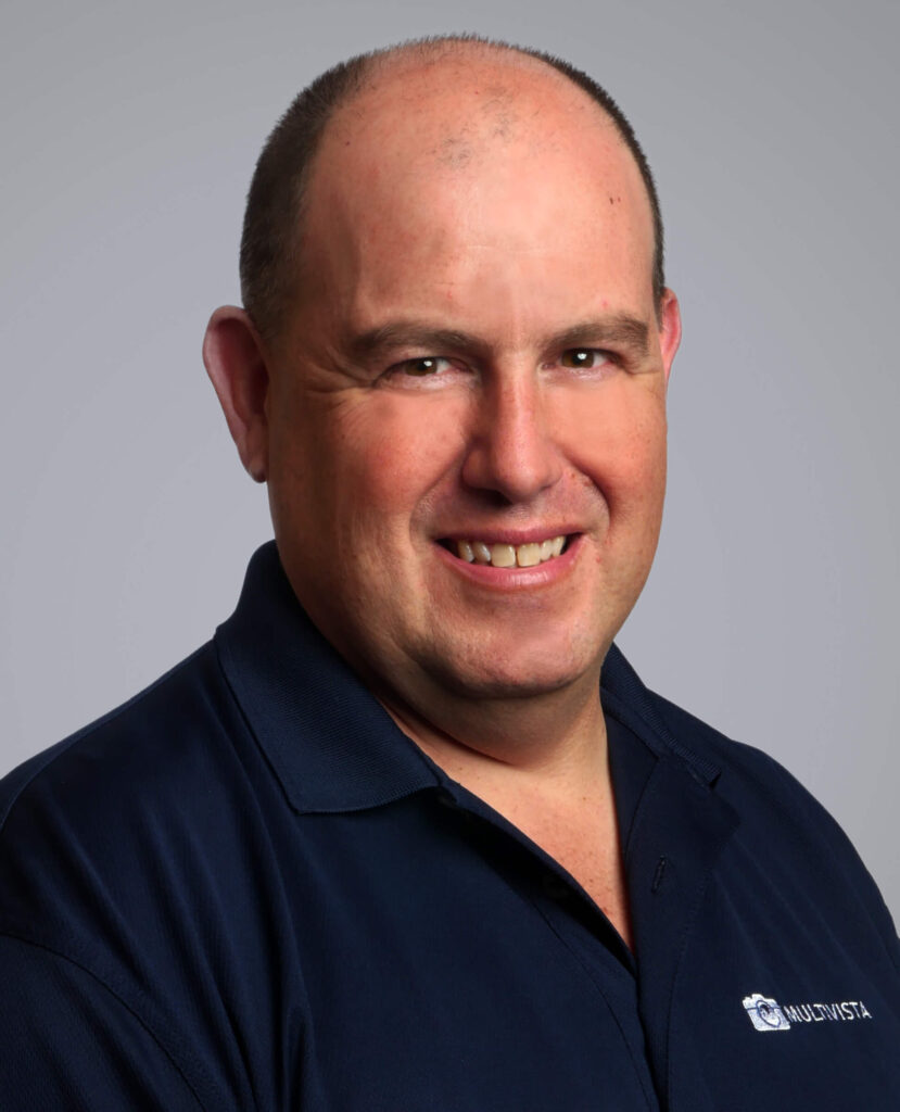 Headshot of a smiling man in a navy polo shirt with a Multivista logo against a grey background.