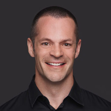 Professional headshot of a smiling man with short dark hair in a black shirt.