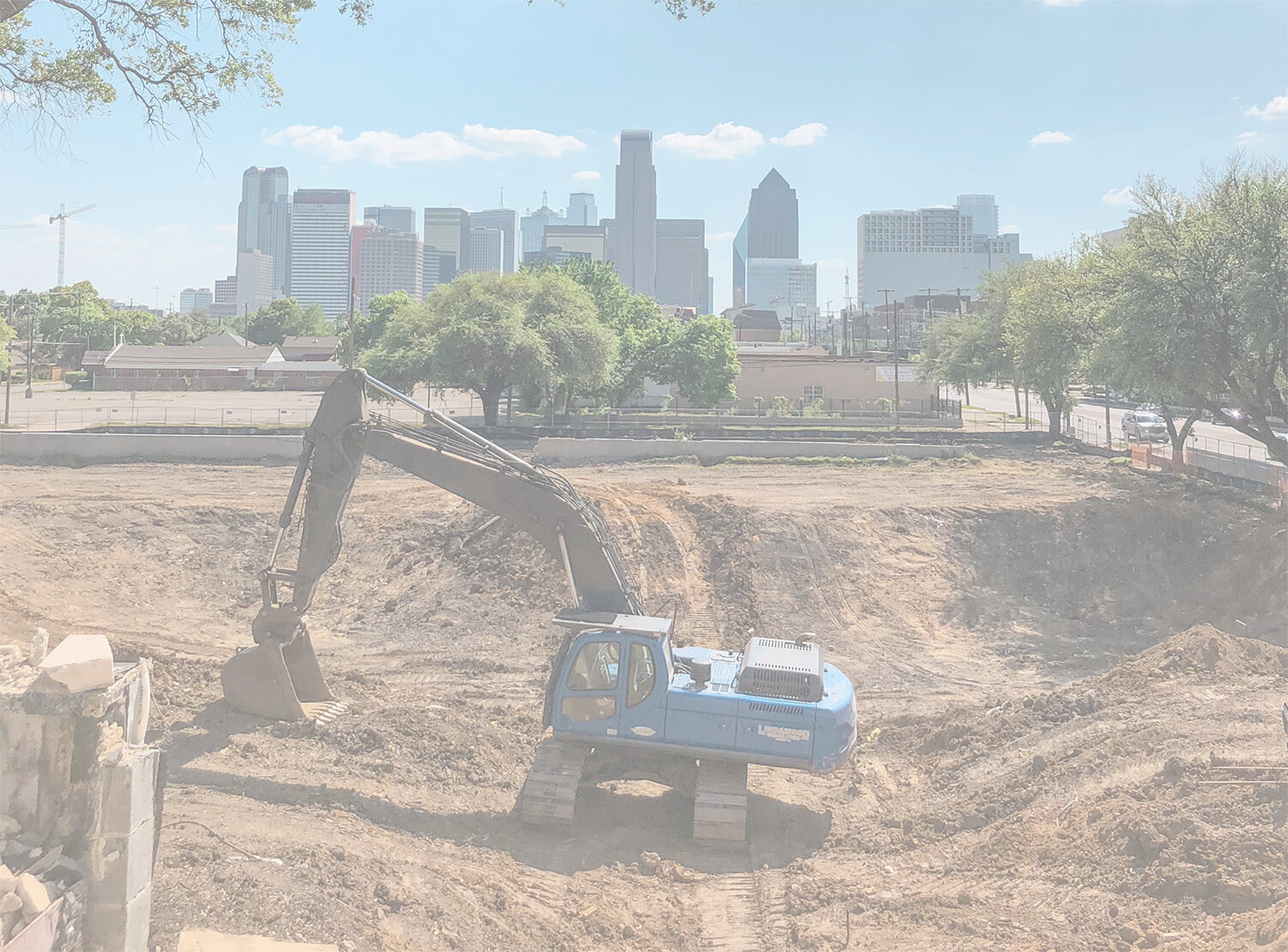 Blue excavator digging dirt on a construction site, with a city skyline in the background.