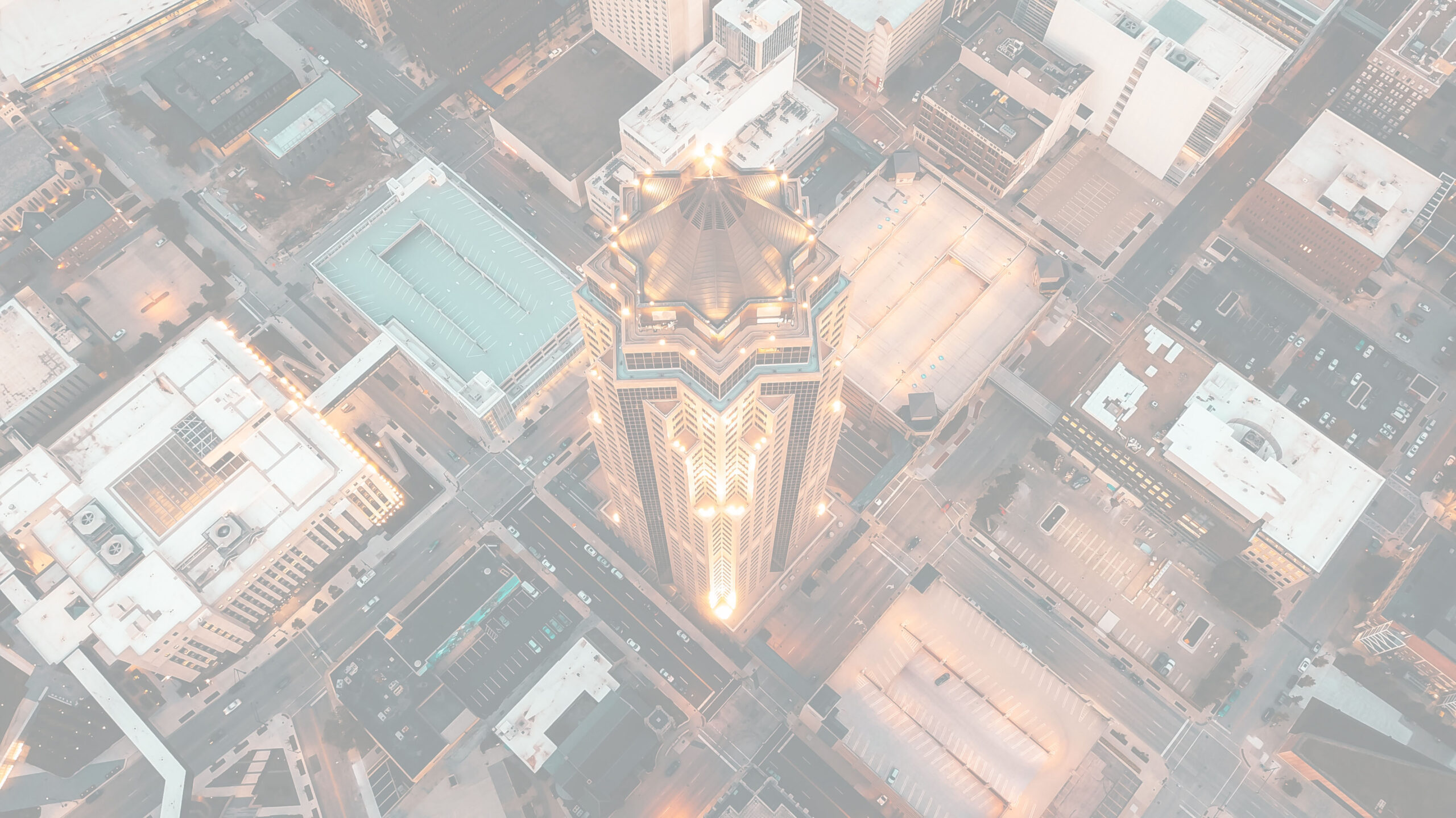 Aerial view of an illuminated skyscraper at night, surrounded by city streets and buildings.