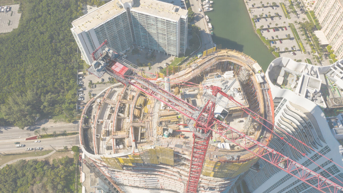 Aerial view of a curved high-rise building construction site with a red tower crane, urban development in progress.