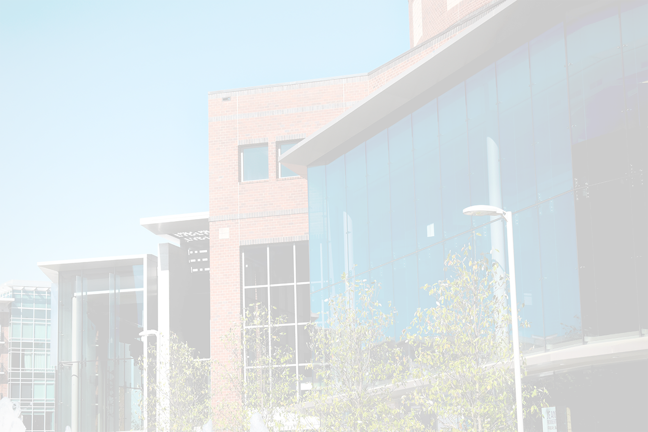 Modern building with brick and large glass facades against a blue sky, with trees and a street light.