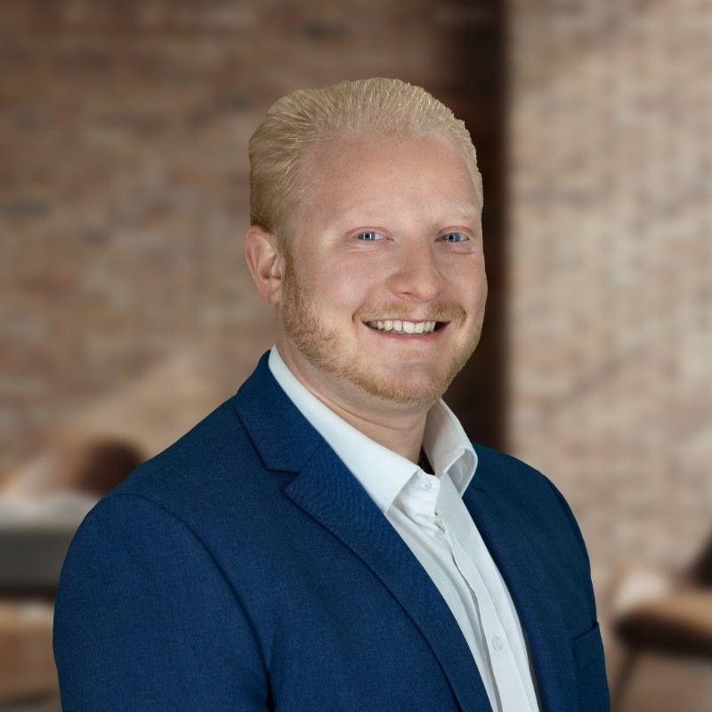 Professional headshot of a smiling man with blonde hair, beard, and blue suit jacket.