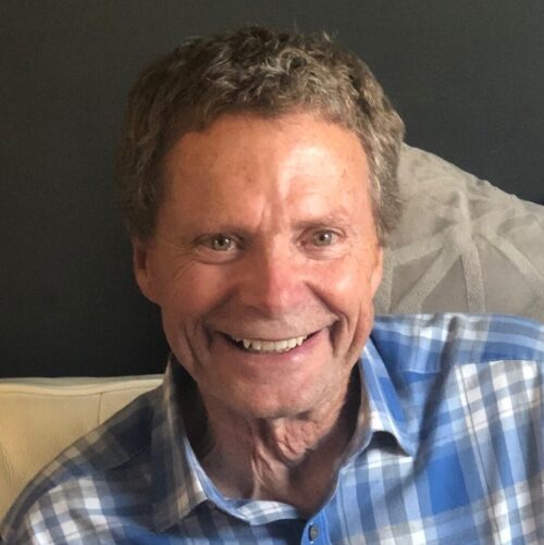 Headshot of a smiling man with curly brown hair in a blue plaid shirt.